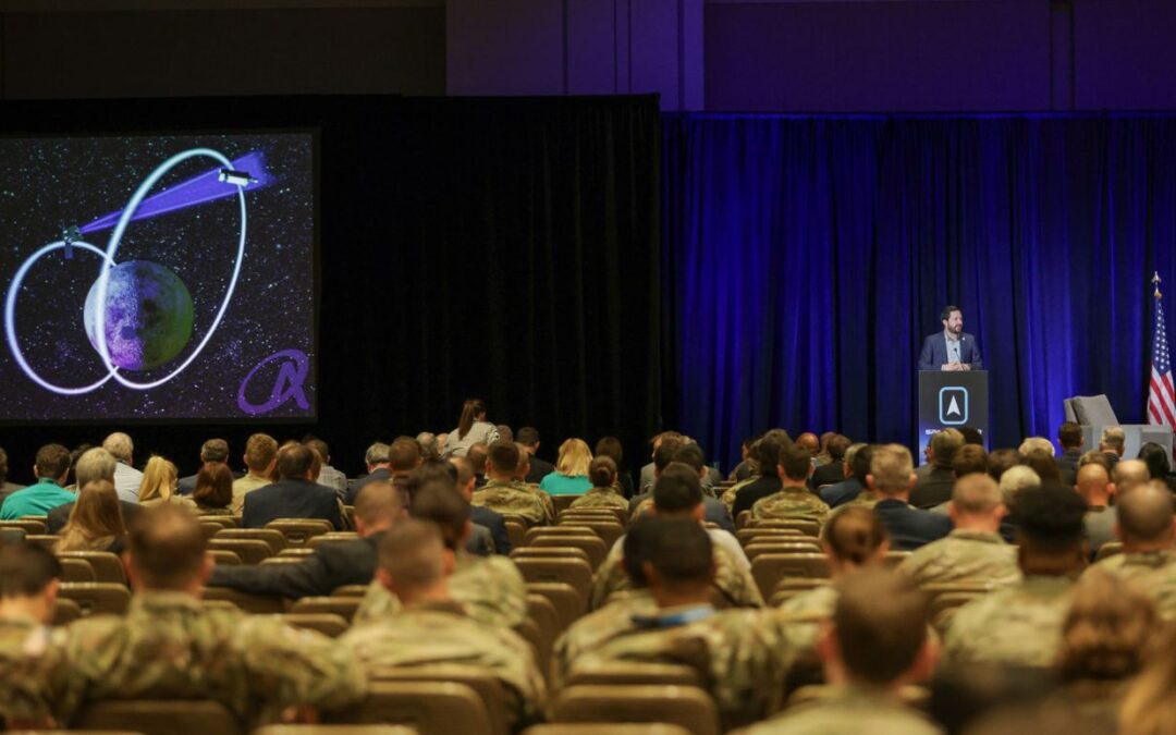 Brad Cheetham presents on the Oracle program to an auditorium of people in US military uniform.